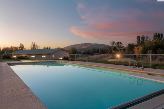 pool at dusk featuring fence, a mountain view, and a fenced in pool