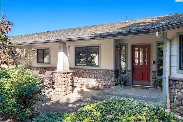 doorway to property with stone siding, covered porch, and roof with shingles