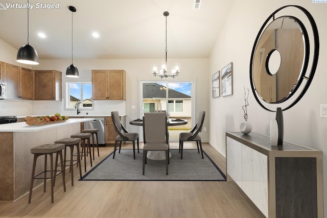 dining area with lofted ceiling, sink, an inviting chandelier, and light hardwood / wood-style flooring