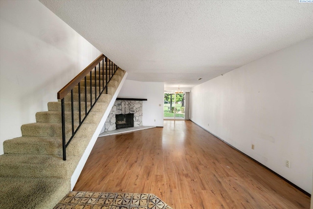 unfurnished living room with wood finished floors, stairway, a textured ceiling, a stone fireplace, and a chandelier