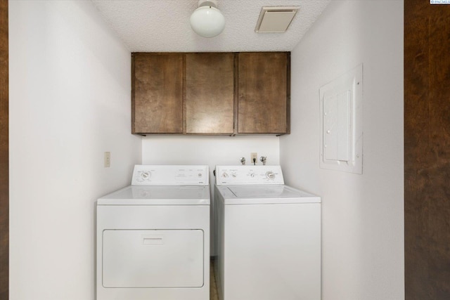 washroom with washing machine and clothes dryer, cabinet space, electric panel, and a textured ceiling