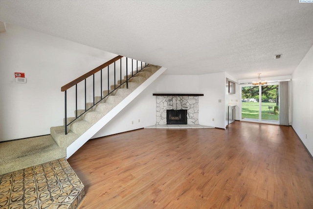 unfurnished living room with wood finished floors, a chandelier, stairs, a textured ceiling, and a stone fireplace