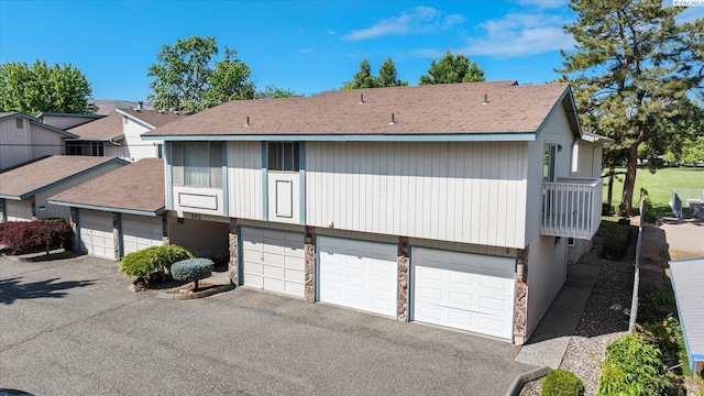 rear view of property featuring stone siding, asphalt driveway, and an attached garage