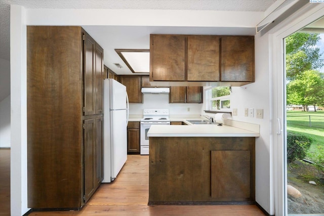 kitchen featuring white appliances, under cabinet range hood, a peninsula, light wood-type flooring, and light countertops