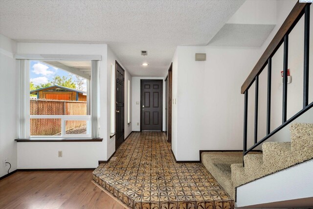 foyer with wood finished floors, a textured ceiling, stairway, and baseboards