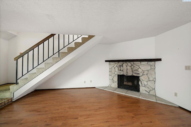unfurnished living room with wood finished floors, stairs, a textured ceiling, and a stone fireplace