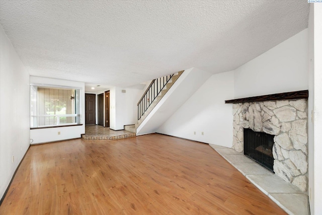 unfurnished living room with a textured ceiling, a fireplace, wood finished floors, stairway, and baseboards