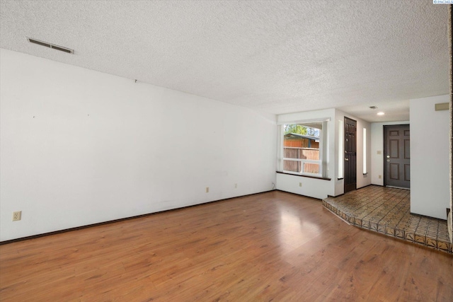 unfurnished living room with wood finished floors, a textured ceiling, and baseboards
