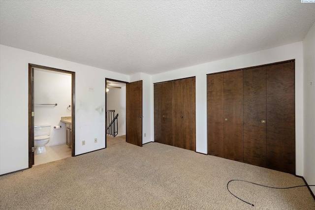 unfurnished bedroom with two closets, light colored carpet, ensuite bathroom, and a textured ceiling