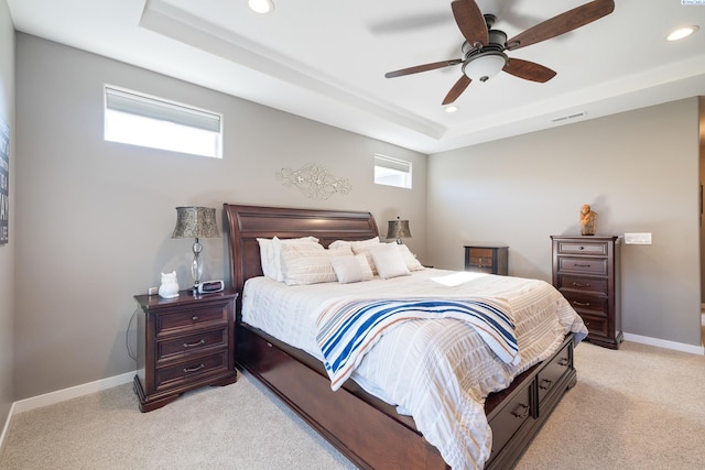 bedroom featuring light carpet, visible vents, baseboards, a tray ceiling, and multiple windows