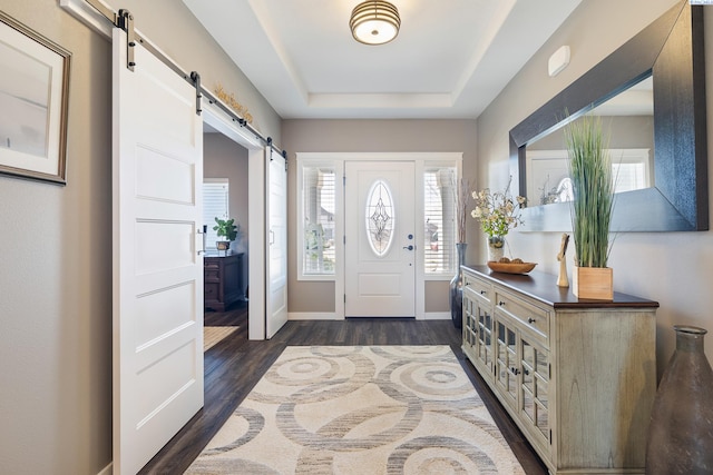 foyer entrance with baseboards, a barn door, a tray ceiling, and dark wood-style flooring