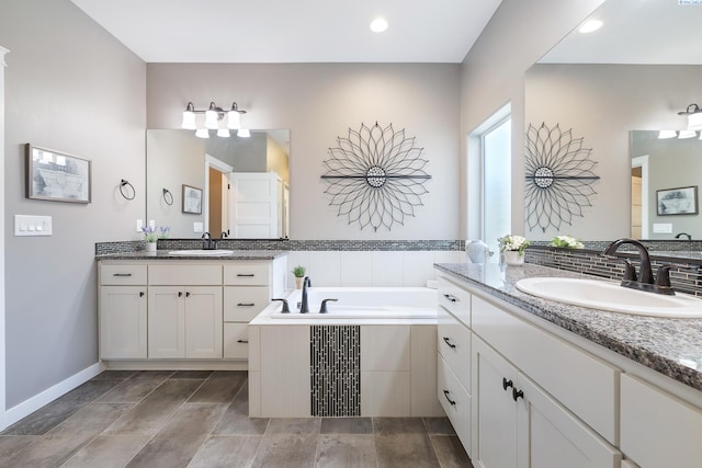 full bathroom featuring a bath, baseboards, two vanities, and a sink