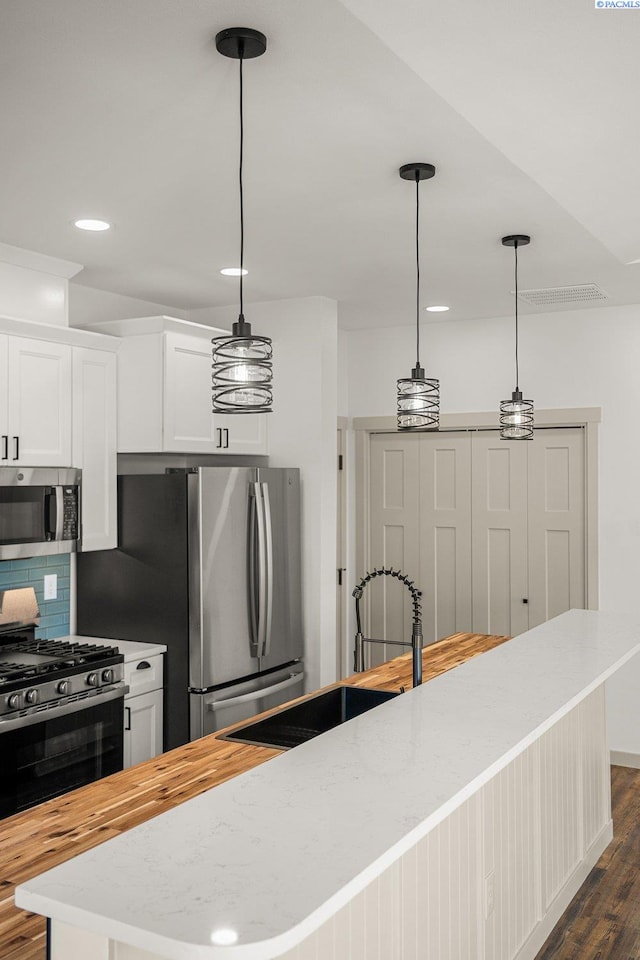 kitchen featuring stainless steel appliances, decorative light fixtures, dark hardwood / wood-style flooring, and white cabinets