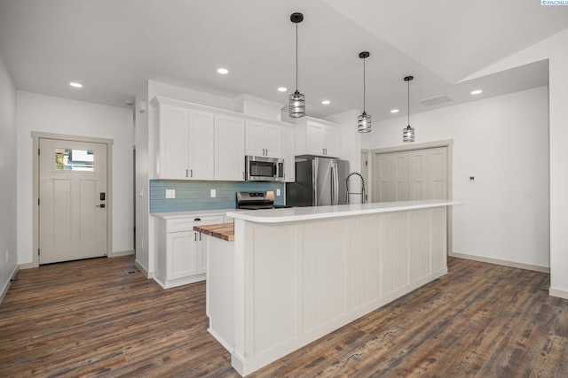 kitchen featuring white cabinets, backsplash, hanging light fixtures, stainless steel appliances, and a center island with sink