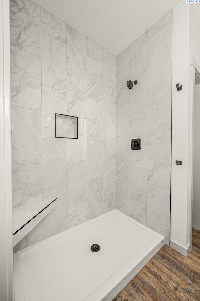 bathroom featuring a tile shower and wood-type flooring