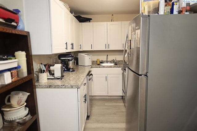 kitchen featuring appliances with stainless steel finishes, white cabinetry, sink, light stone countertops, and light hardwood / wood-style flooring