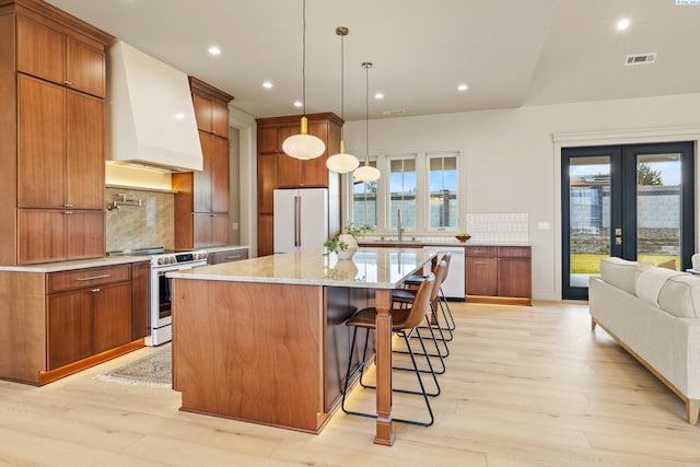 kitchen featuring sink, decorative light fixtures, custom range hood, white appliances, and a large island