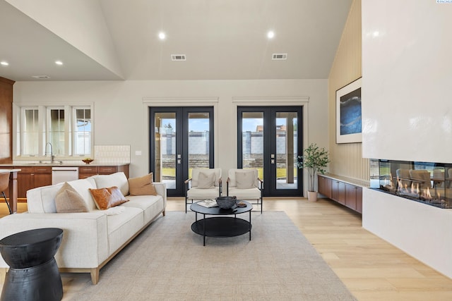 living room with a multi sided fireplace, high vaulted ceiling, sink, light hardwood / wood-style floors, and french doors