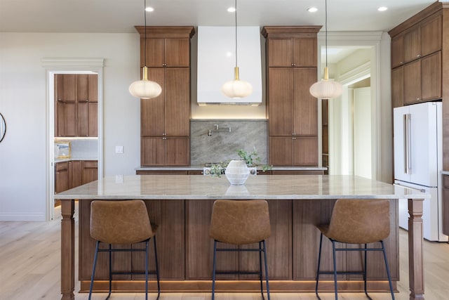 kitchen featuring a spacious island, light stone counters, hanging light fixtures, white refrigerator, and a kitchen breakfast bar