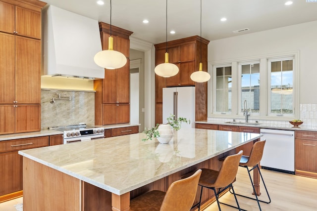 kitchen featuring premium range hood, a spacious island, sink, white appliances, and light stone countertops