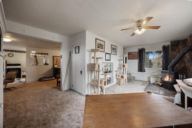 carpeted living room featuring ceiling fan and a wood stove