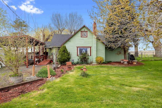 view of front of property featuring a front yard, a chimney, a shingled roof, and fence