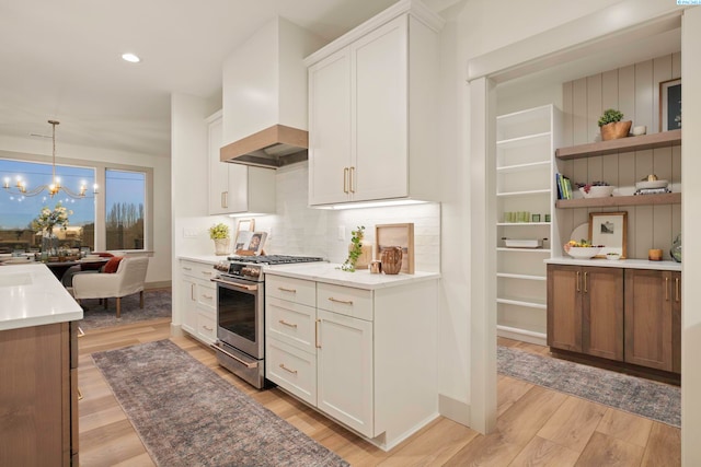 kitchen featuring decorative light fixtures, stainless steel gas range, custom exhaust hood, and white cabinets