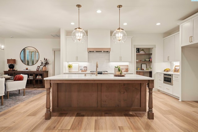 kitchen with custom exhaust hood, a center island with sink, pendant lighting, and white cabinets