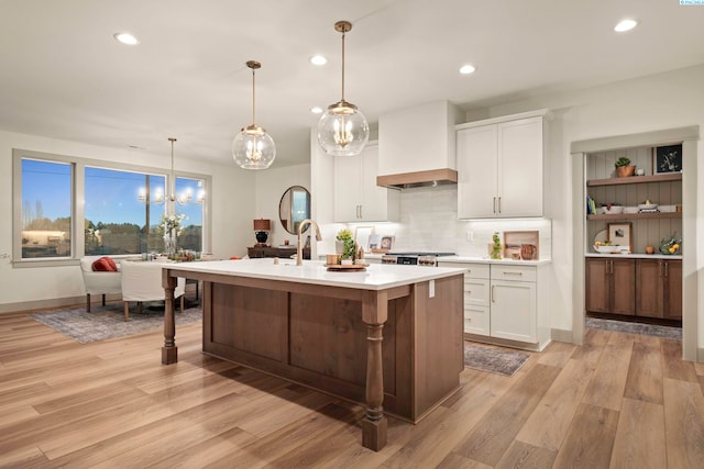 kitchen featuring a center island with sink, decorative light fixtures, custom exhaust hood, and white cabinets