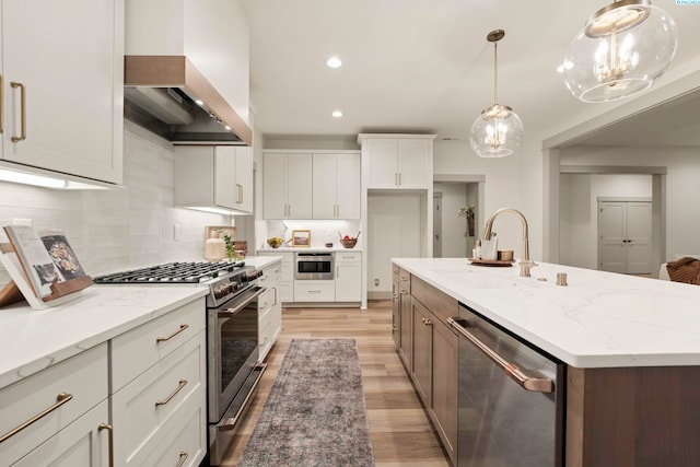 kitchen featuring custom exhaust hood, white cabinetry, appliances with stainless steel finishes, an island with sink, and pendant lighting