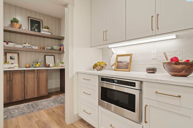 kitchen featuring light stone counters, tasteful backsplash, white cabinets, oven, and light wood-type flooring