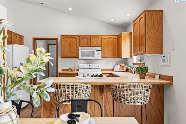 2418 S Arthur Ct, Kennewick, WA 99338 - kitchen with white appliances, lofted ceiling, a peninsula, light countertops, and brown cabinetry