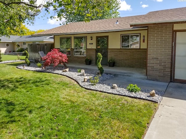 view of front facade featuring brick siding, a shingled roof, fence, a patio area, and a front yard