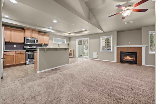 kitchen featuring light colored carpet, stainless steel appliances, a breakfast bar, and a raised ceiling