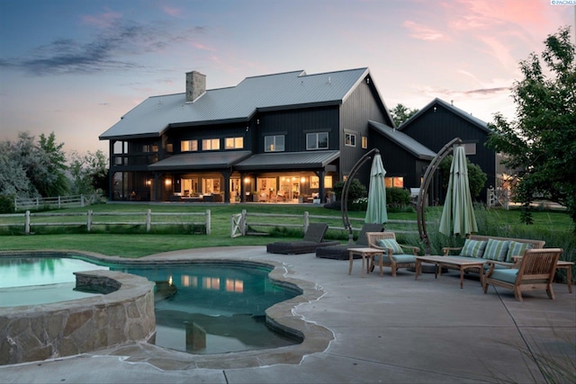 back of property at dusk featuring a patio area, a chimney, a lawn, and an outdoor hangout area