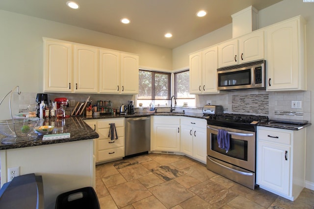 kitchen with white cabinetry, appliances with stainless steel finishes, sink, and dark stone countertops