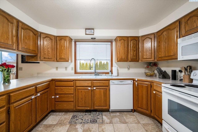 kitchen with white appliances, brown cabinetry, a sink, and light countertops