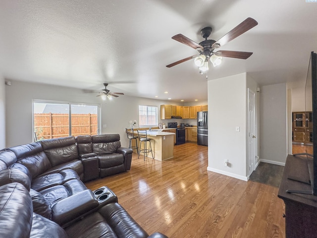 living room with ceiling fan, a textured ceiling, and light wood-type flooring