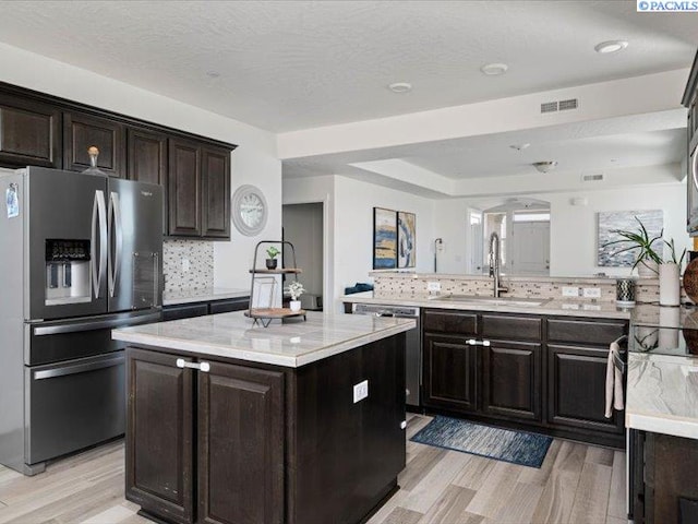 kitchen featuring visible vents, a center island, stainless steel appliances, light wood-type flooring, and a sink