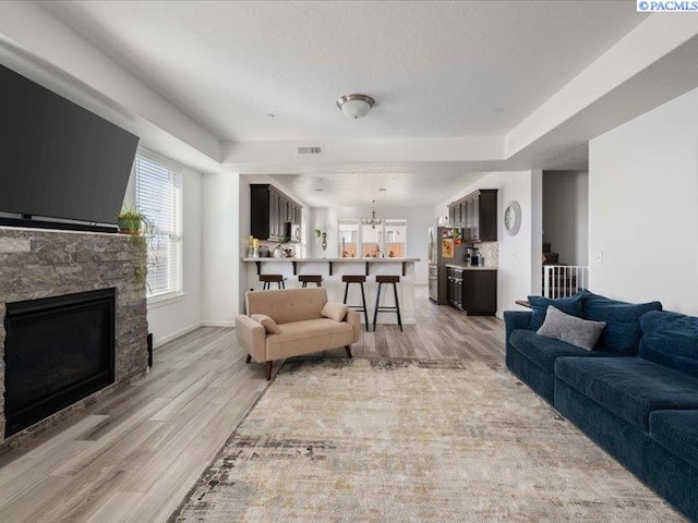 living room with a fireplace, visible vents, light wood-style floors, a textured ceiling, and baseboards