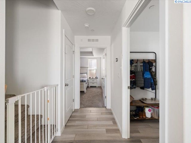 corridor with wood finish floors, visible vents, and baseboards