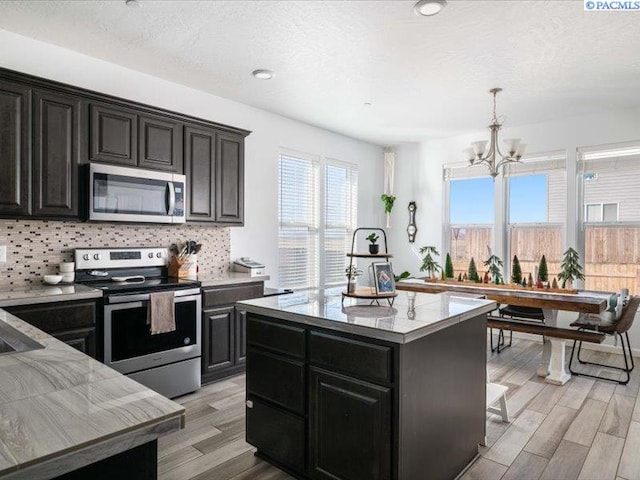 kitchen featuring a notable chandelier, backsplash, appliances with stainless steel finishes, dark cabinets, and light wood-type flooring