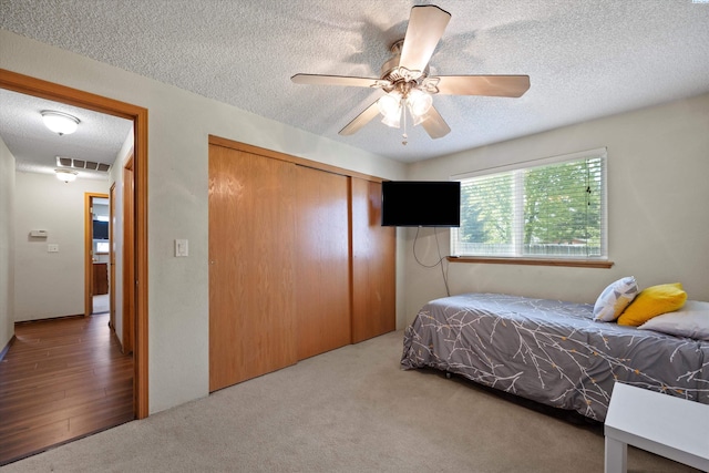 bedroom featuring carpet, visible vents, a ceiling fan, a closet, and a textured ceiling