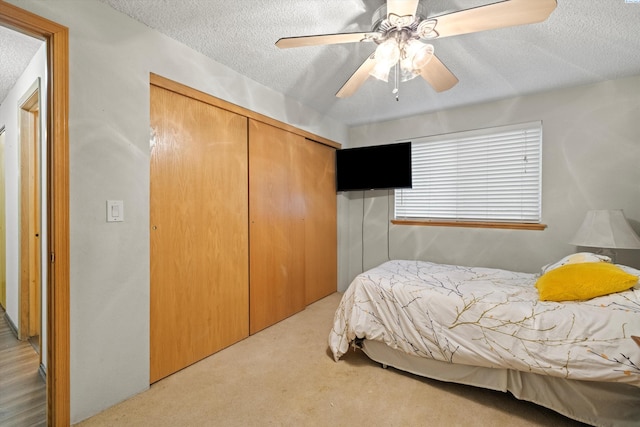 carpeted bedroom with ceiling fan, a closet, and a textured ceiling