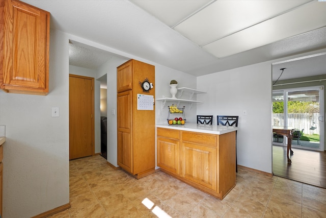 kitchen featuring brown cabinetry, baseboards, open shelves, and light countertops