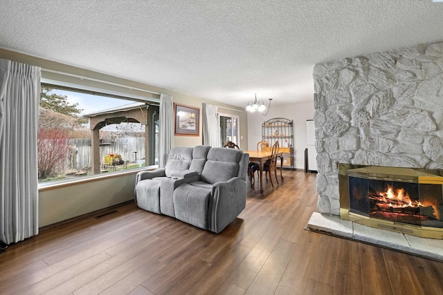 living room with a stone fireplace, a chandelier, hardwood / wood-style floors, and a textured ceiling