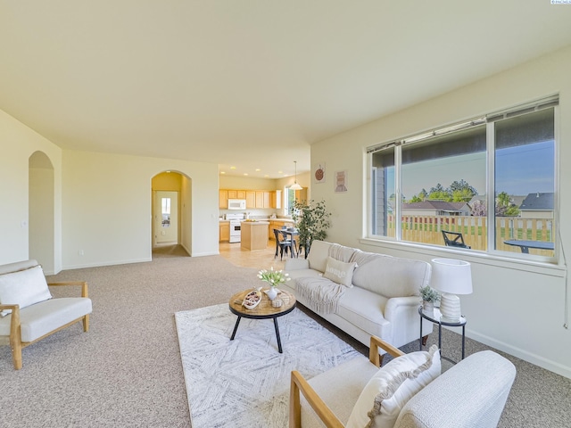 living area featuring arched walkways, baseboards, and light colored carpet
