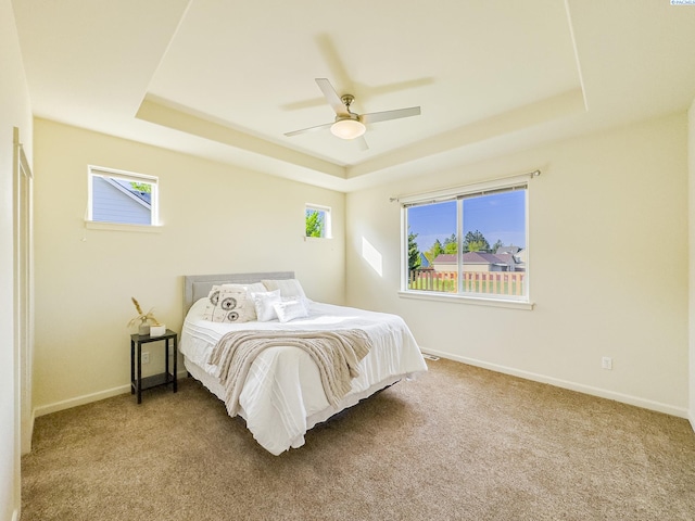 bedroom with ceiling fan, baseboards, a tray ceiling, and carpet
