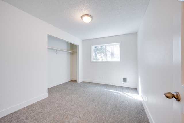 unfurnished bedroom with a textured ceiling, visible vents, carpet floors, baseboards, and a closet