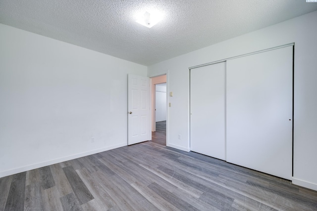 unfurnished bedroom with baseboards, a textured ceiling, wood finished floors, and a closet